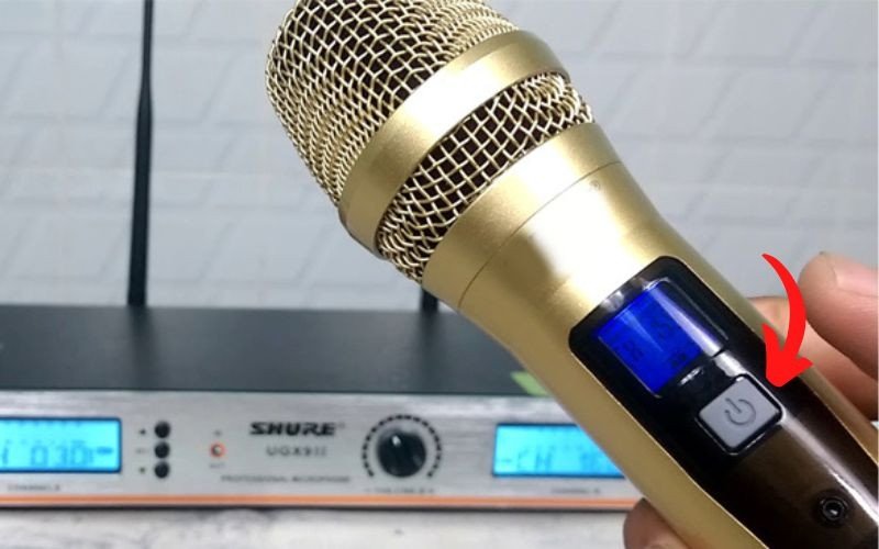 Người dùng đang nhấn nút nguồn để khởi động micro không dây, bước đầu tiên trong cách kết nối micro không dây với loa bluetooth.