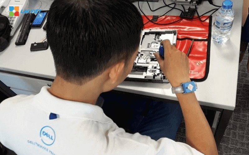 Hình ảnh cận cảnh một kỹ thuật viên đang tháo nắp lưng laptop Dell để chuẩn bị nâng cấp, với các dụng cụ cần thiết xung quanh