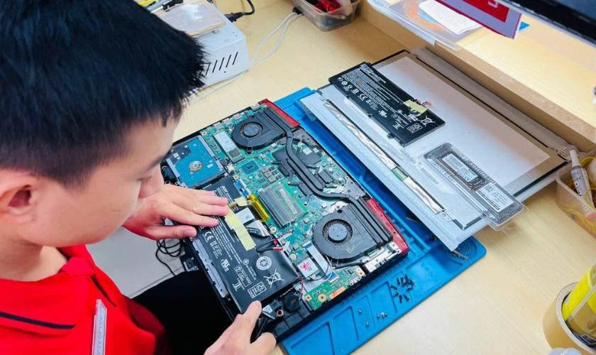 Kỹ thuật viên đang kiểm tra bên trong một chiếc laptop, chuẩn bị cho việc thay thế hoặc sửa chữa pin