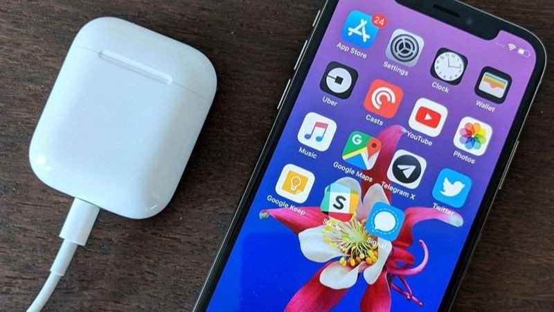 Một bàn tay đặt tai nghe Bluetooth vào hộp sạc đang hiển thị đèn báo sạc