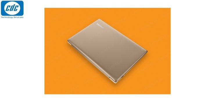 Một chiếc laptop Lenovo Ideapad màu hồng vàng đặt trên bàn, phía sau là không gian làm việc hiện đại