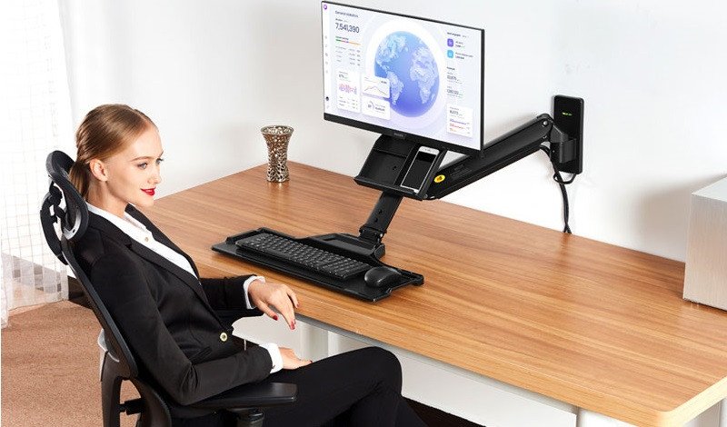 Một cô gái đang làm việc trước bàn làm việc được trang bị giá treo màn hình PC gắn tường giúp tiết kiệm không gian