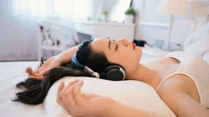 Một người đàn ông đang đeo tai nghe khi ngủ, đặt ra câu hỏi về các cách tối ưu việc đeo tai nghe để bảo vệ sức khỏe.