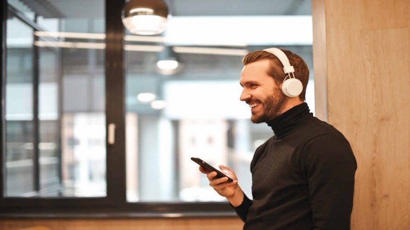 Người dùng đang nhấn giữ nút nguồn trên tai nghe Bluetooth kiểu vòng cổ để thực hiện reset